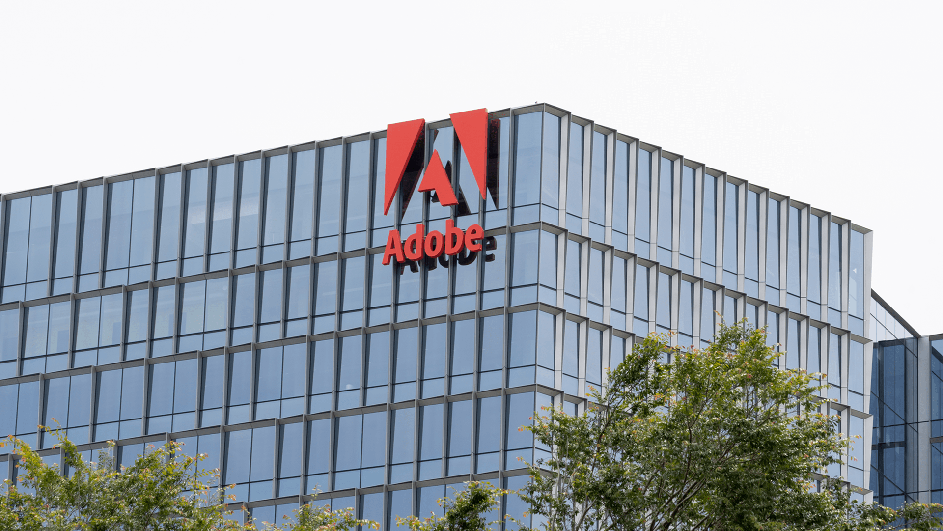 Modern office building with large glass windows and a prominent red Adobe logo near the top corner.